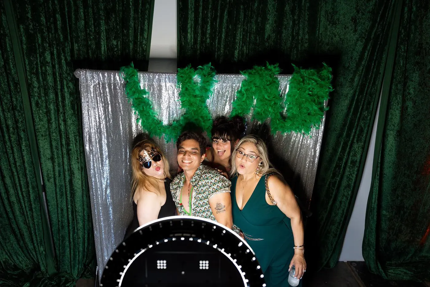 Guests in novelty glasses in front of a greenery wall photo booth